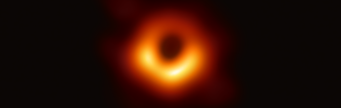 An image of a black hole, showing a dark central region (the event horizon) surrounded by a glowing, ring-like structure of bright orange and yellow light. This iconic image represents the first-ever photograph of a black hole, captured by the Event Horizon Telescope